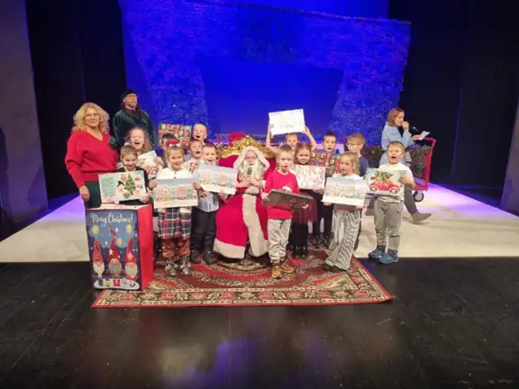 Dzieci z klasy pierwszej b pozuja do zdjecia z Mikołajem na scenie Teatru Lalek Pleciuga
