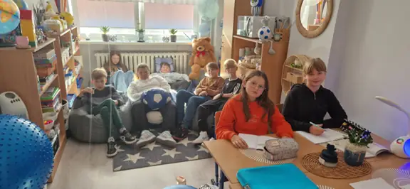 Uczniowie siedzący na podłodze i przy stole w gabinecie pedagoga.