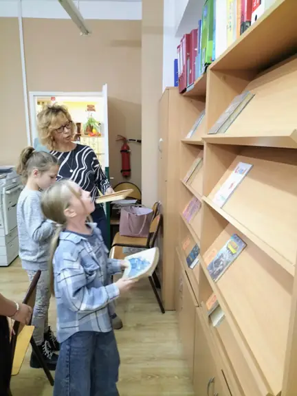 Dzieci układają książki na półkach zgodnie z oznaczeniami działowymi.