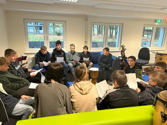 Uczniowie siedzą na kanapach i uczą się tekstu piosenki.