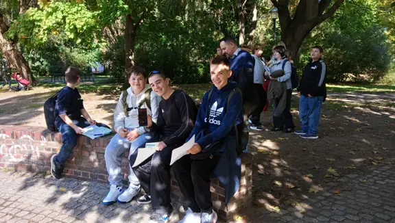 Mała grupka uczniów siedzi na murku w parku.