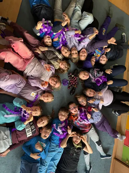 Uczniowie leżą na dywanie ubrani w kolor fioletowy