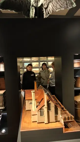 Troje uczniów ogląda eksponat w muzeum, z przodu zdjęcia widać makietę budynku.