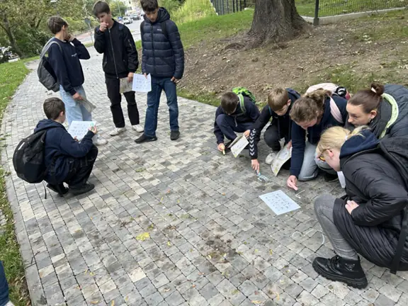 grupka uczniów pisze kredą na ziemi swoje imiona w języku hebrajskim