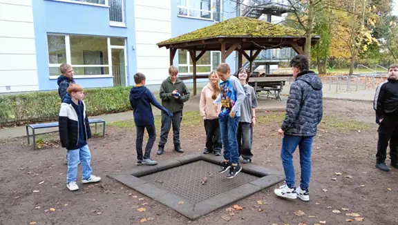 Uczniowie przed szkołą rozmawiają i skaczą na trampolinie