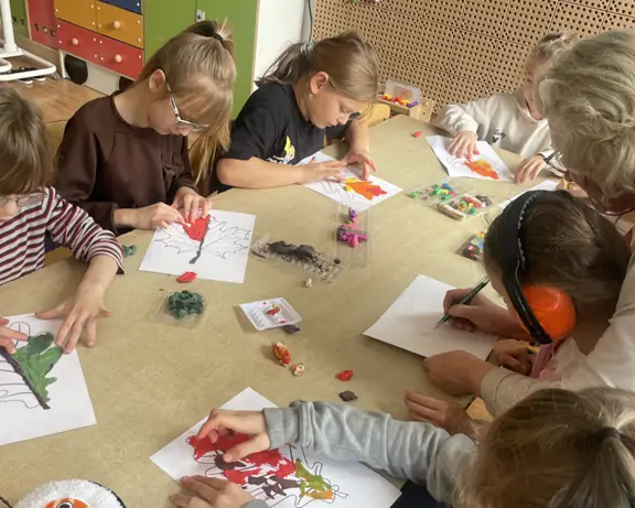 Wychowankowie świetlicy szkolnej kolorują listki metodą rozcierania plasteliny.