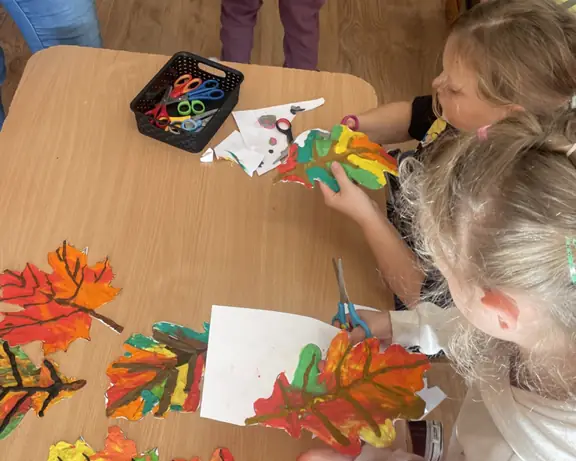 Dwie uczennice świetlicy wycinające wykonane przez siebie listki.