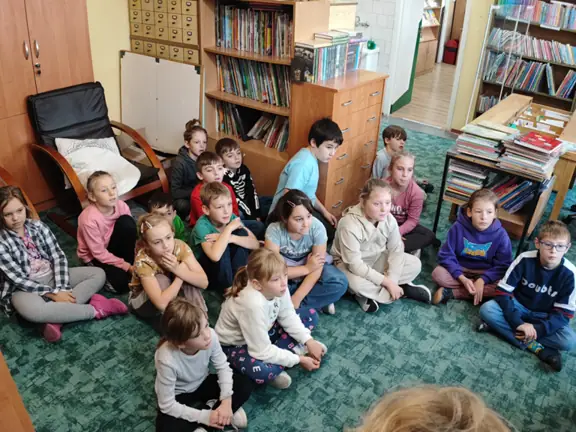 Uczniowie kl. II b siedzą na dywanie w bibliotece.