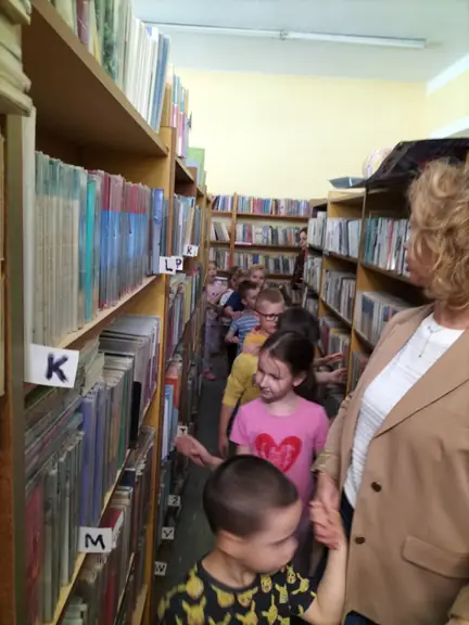 Przedszkolaki z grupy Kotki spacerują między bibliotecznymi regałami.