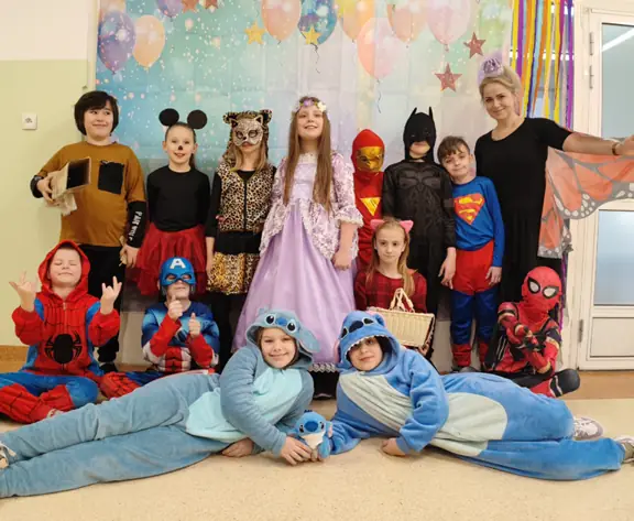 Uczniowie klasy 2b z wychowawcą, pozują do zdjęcia w strochach karnawałowych.