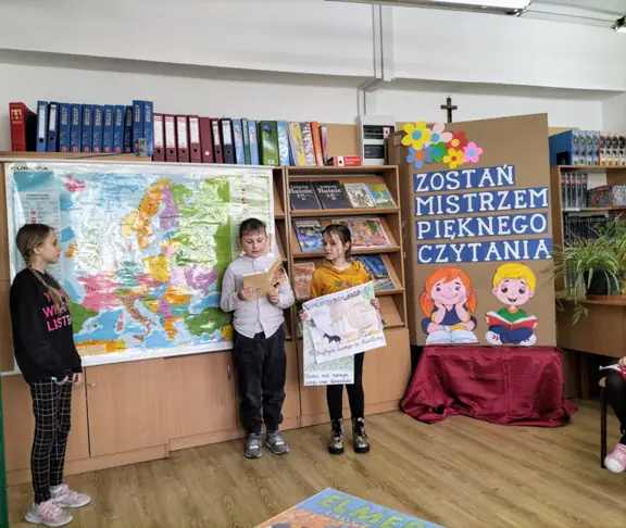 Uczeń z kl. IIIc czyta fragment bajki, jego koleżanki prezentują klasową książeczkę oraz mapę Europy.