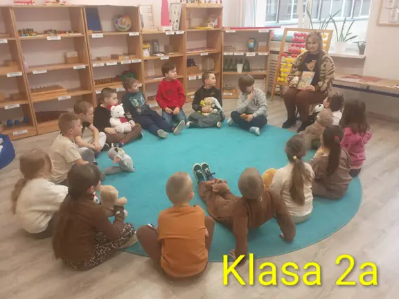 Uczniowie klasy 2a siedzą w kręgu i przedstawiaja klasie swoje misie.