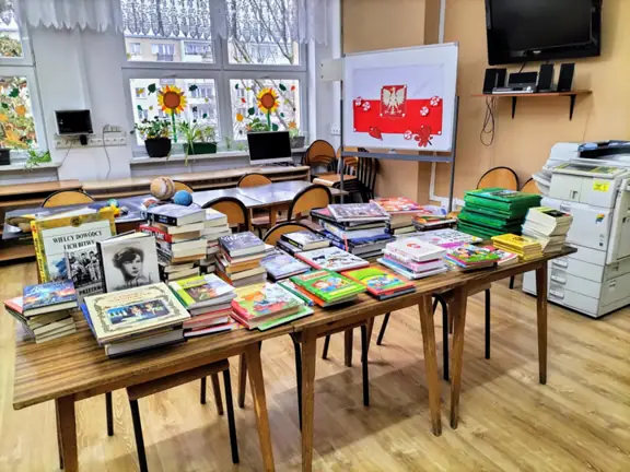 Na stolikach w czytelni szkolnej leżą zebrane podczas zbiórki książki.