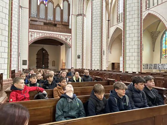 grupa polsko-niemiecka jest w katedrze, siedzą w ławkach kościelnych i podziwiają wnętrze budowli.