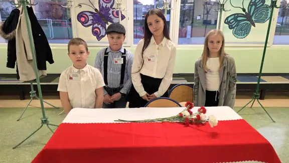 Czworo uczniów witających gości przy stoliku z barwami narodowymi