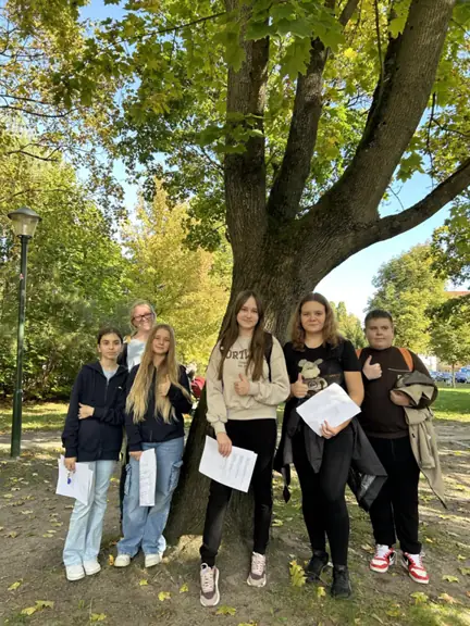 Sześciu uczniów pozuje do wspólnego zdjęcia w parku, pod drzewem.