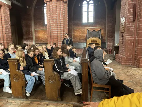 Uczniowie znajdują się w kościele, siedzą w ławkach i podziwiają kościół.