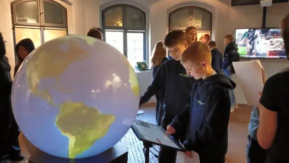 Dwóch uczniów z Niemiec rozwiązuje zadania w muzeum, stojąc przy globusie