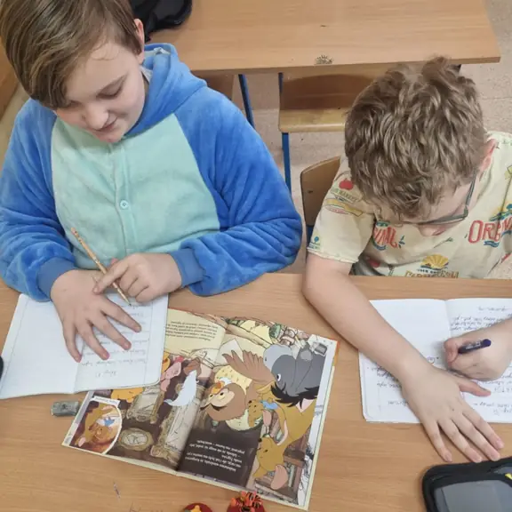 Chłopcy zapisują w zeszytach informacje o bohaterach bajki.