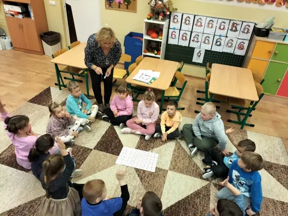 Pani bibliotekarka wyjaśnia przedszkolakom z grupy 01 na czym polega zadanie.