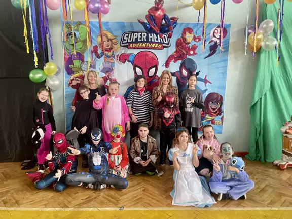 Uczniowie klasy 3c z wychowawcami pozuja do zdjęcia w przebraniach na balu karnawałowym.