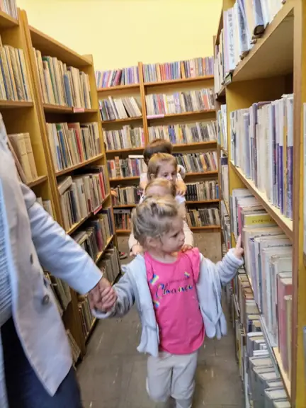 Przedszkolaki oglądają książki ustawione na regałach w bibliotece.