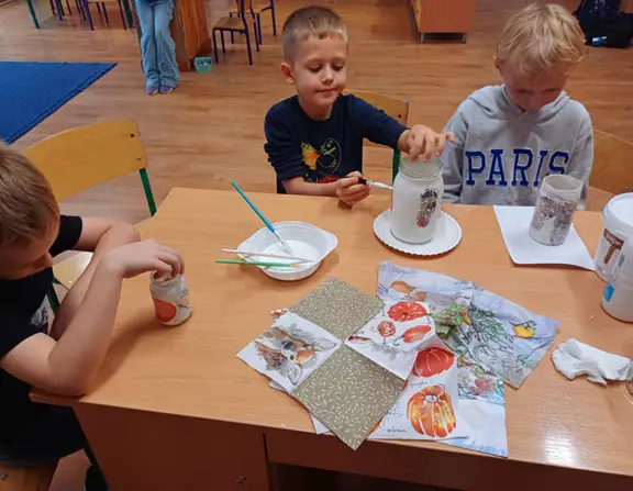 uczniowie nakładają elementy z serwetek przy pomocy pędzelków i kleju