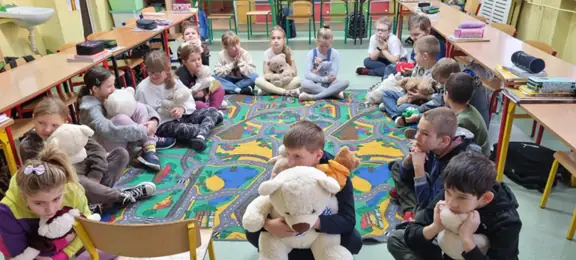 Dzieci z kl. IIIa siedzą na dywanie z misiami.
