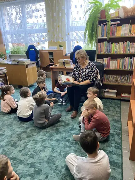 Dzieci siedzą na dywanie i słuchają czytanej przez p. bibliotekarkę bajki.