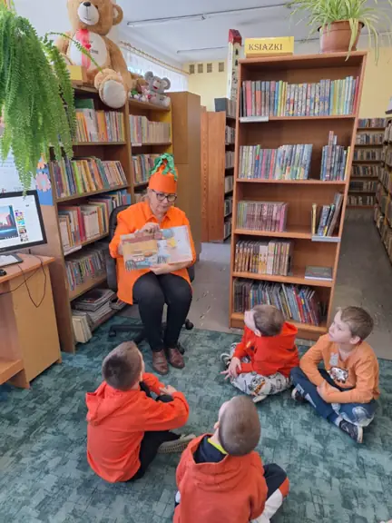 Dzieci z grupy 02 siedzą na dywanie i oglądają ilustracje czytanej im książki.