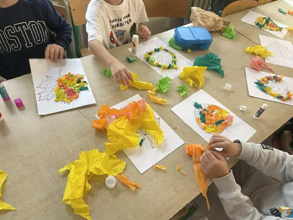 Uczniowie przyklejający kolorową bibułę tworzą jesienne liście