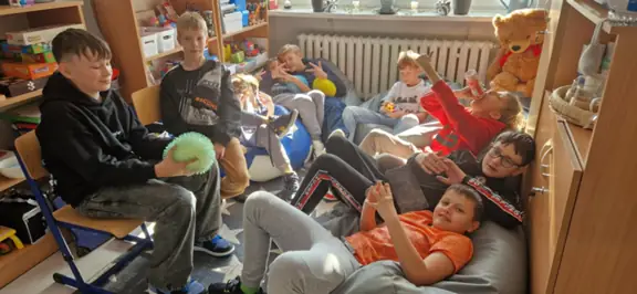 Uczniowie uśmiechają się do aparatu, siedząc na pufach, podłodze.