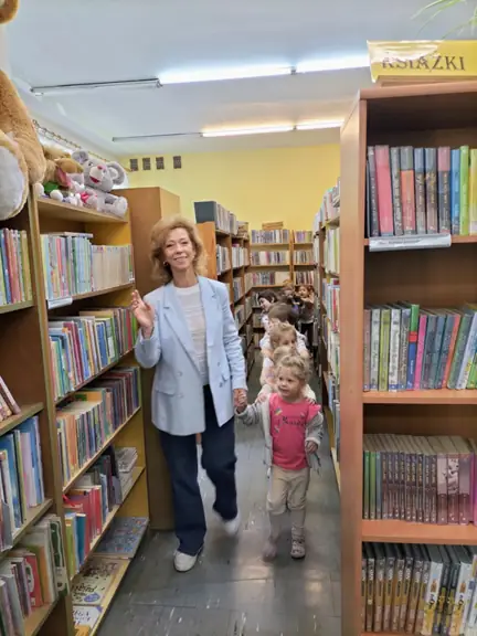 Razem z panią bibliotekarką przedszkolaki spacerują wśród bibliotecznych regałów.