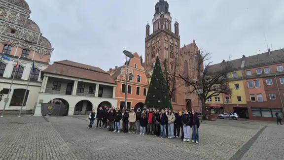 Grupa uczniów pozuje na rynku miasta, przy choince