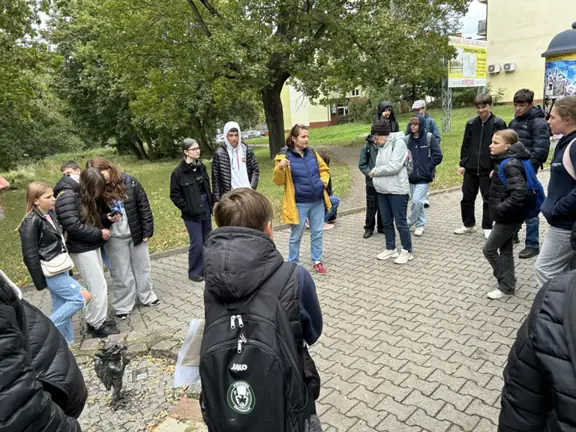 Grupa uczniów stoi dookoła gryfika przy Kościele świętego Ducha i słucha opisu pani przewodnik.