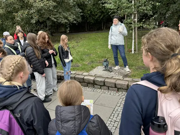 Pani przewodnik stoi przy gryfiku, a przed nią są uczniowie i słuchają opowieści