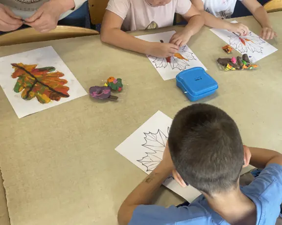 Grupa dzieci rozciera plastelinę na obrysach liści.