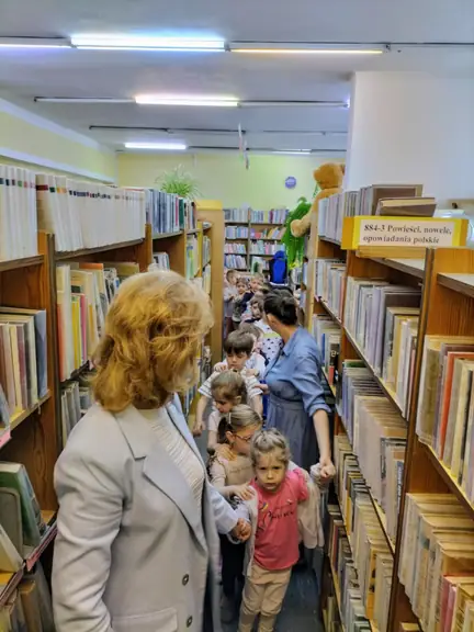Spacer przedszkolaków wśród regałów z książkami.