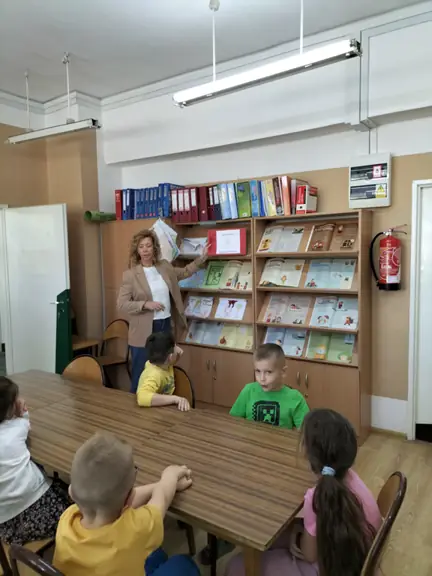 Pani bibliotekarka pokazuje dzieciom książeczki obrazkowe wykonane przez uczniów kl. I-III.