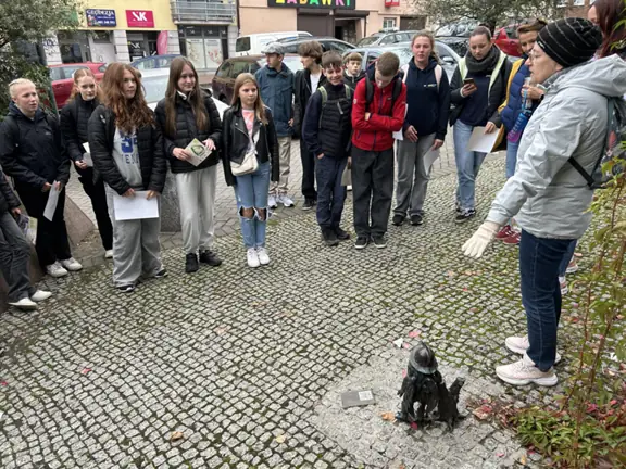 Nauczycielka, pani Renata pokazuje na gryfika, a wokół niej stoją uczniowie i słuchają opisu.