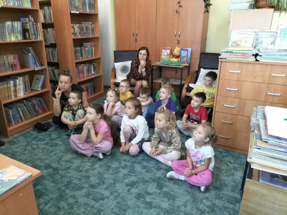 Przedszkolaki siedzą na dywanie i oglądają bajkę relaksacyjną - Przygoda w bibliotece.