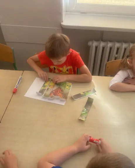 Chłopiec układa i przykleja papierowe puzzle na kartce.