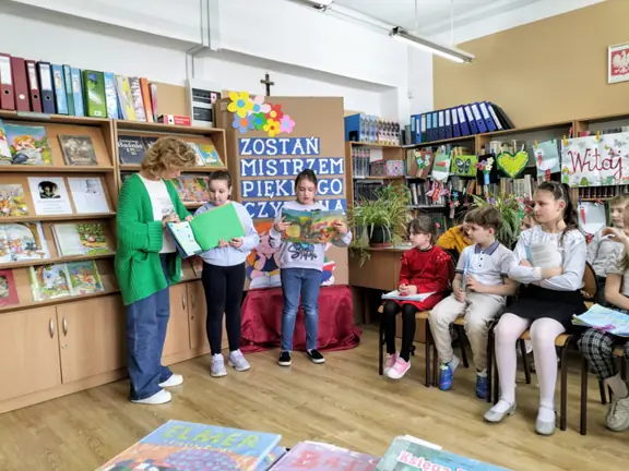 Uczennicz kl. IIa czyta fragment bajki, jej koleżanka prezentuje klasową książeczkę.