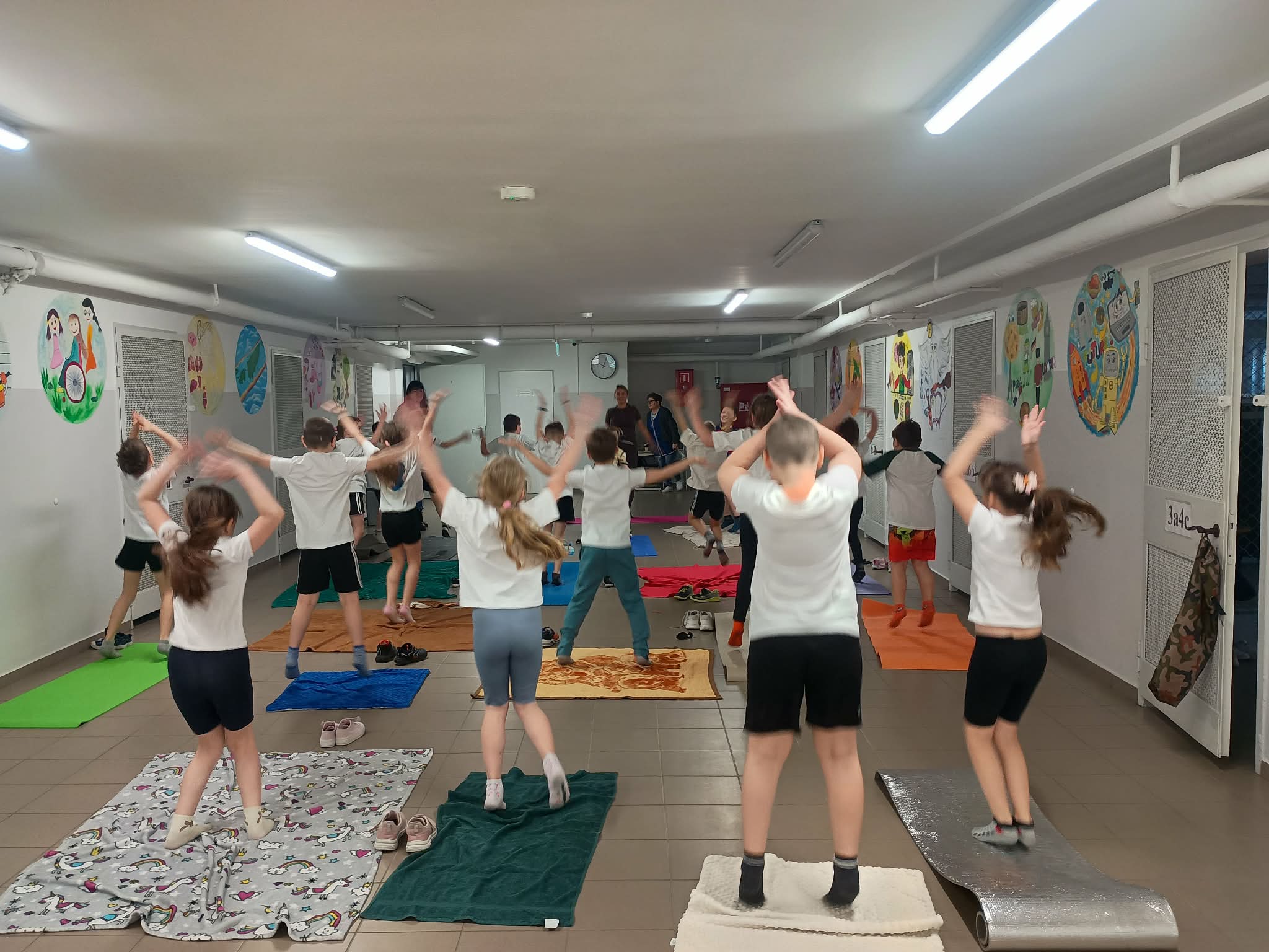 Uczniowie w pozycji stojącej wykonują ćwiczenie na matach i kocach