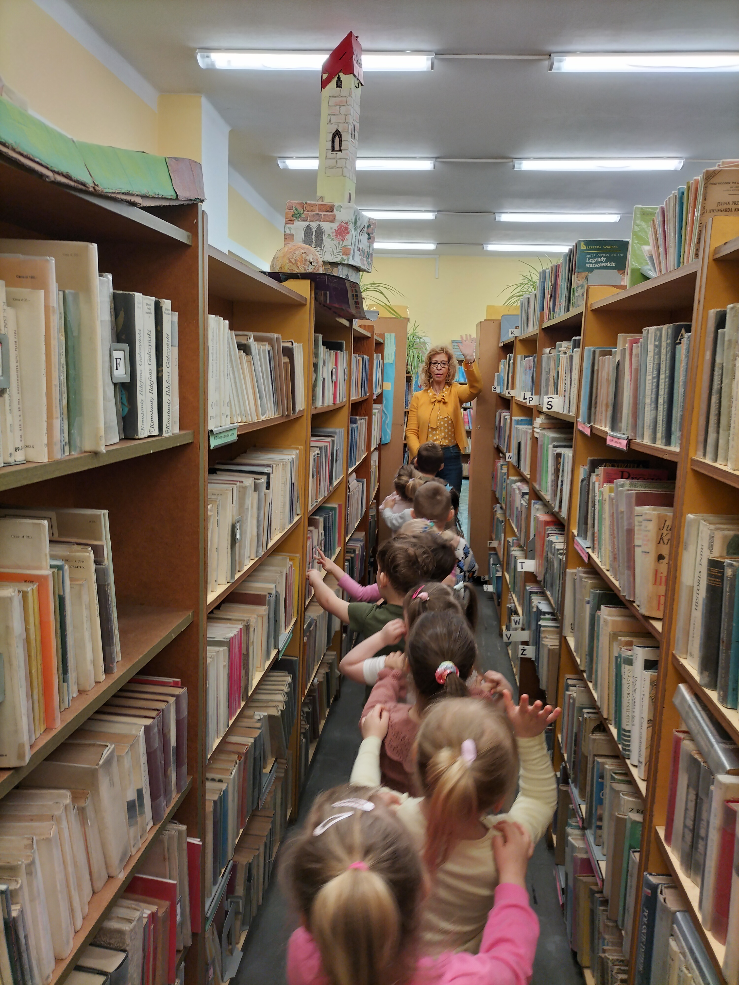 Przedszkolaki spacerują pomiędzy bibliotecznymi regałami