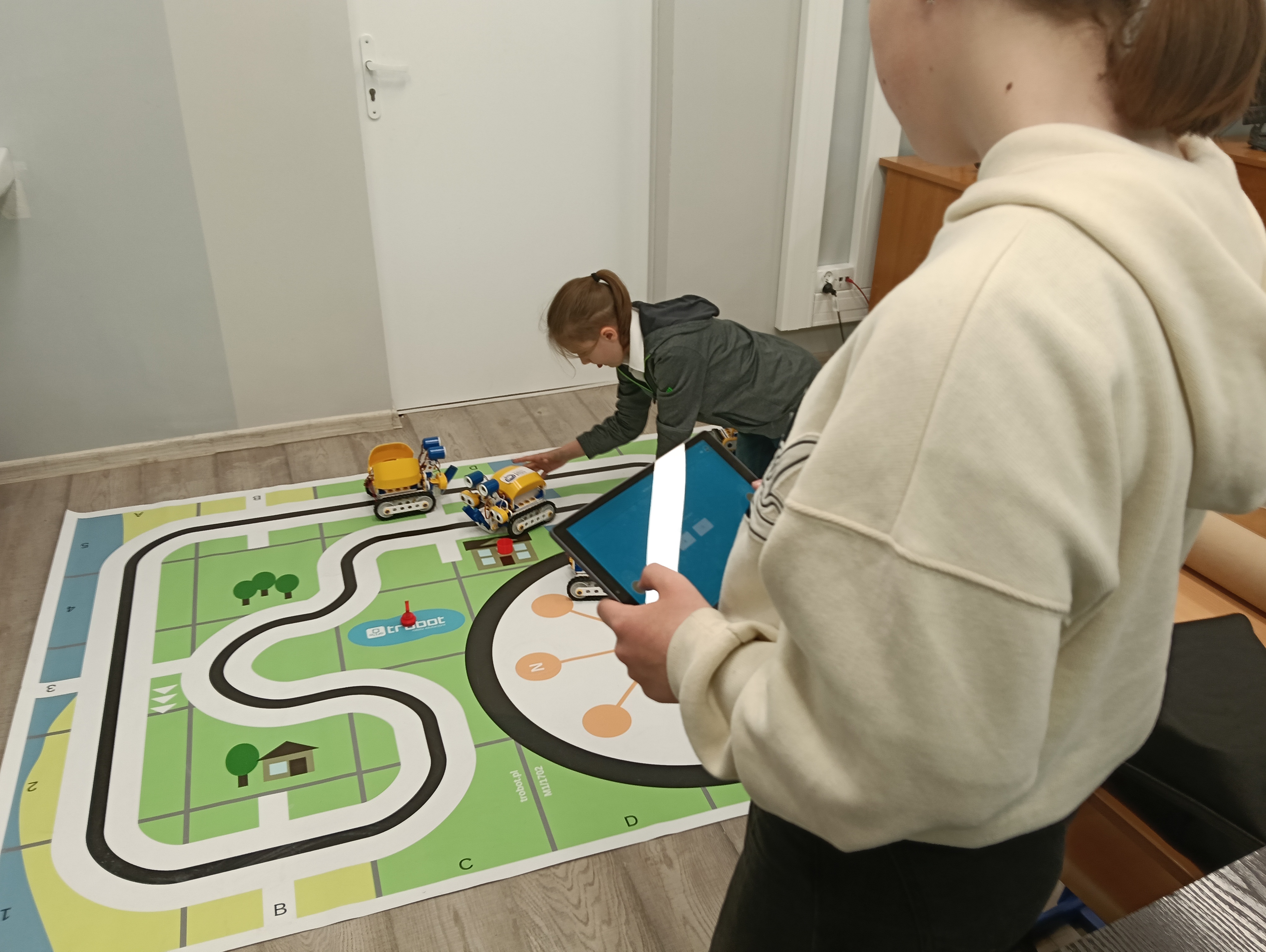 uczniowie sterują robotami SkriBot na specjalnej macie
